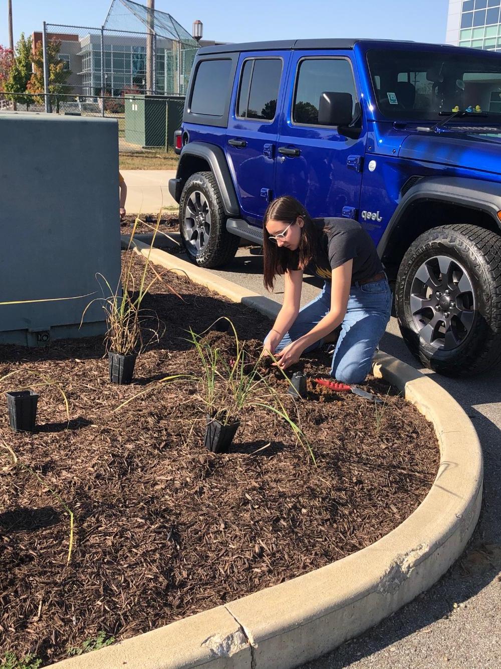 A female geoscience student planting something next to a Jeep