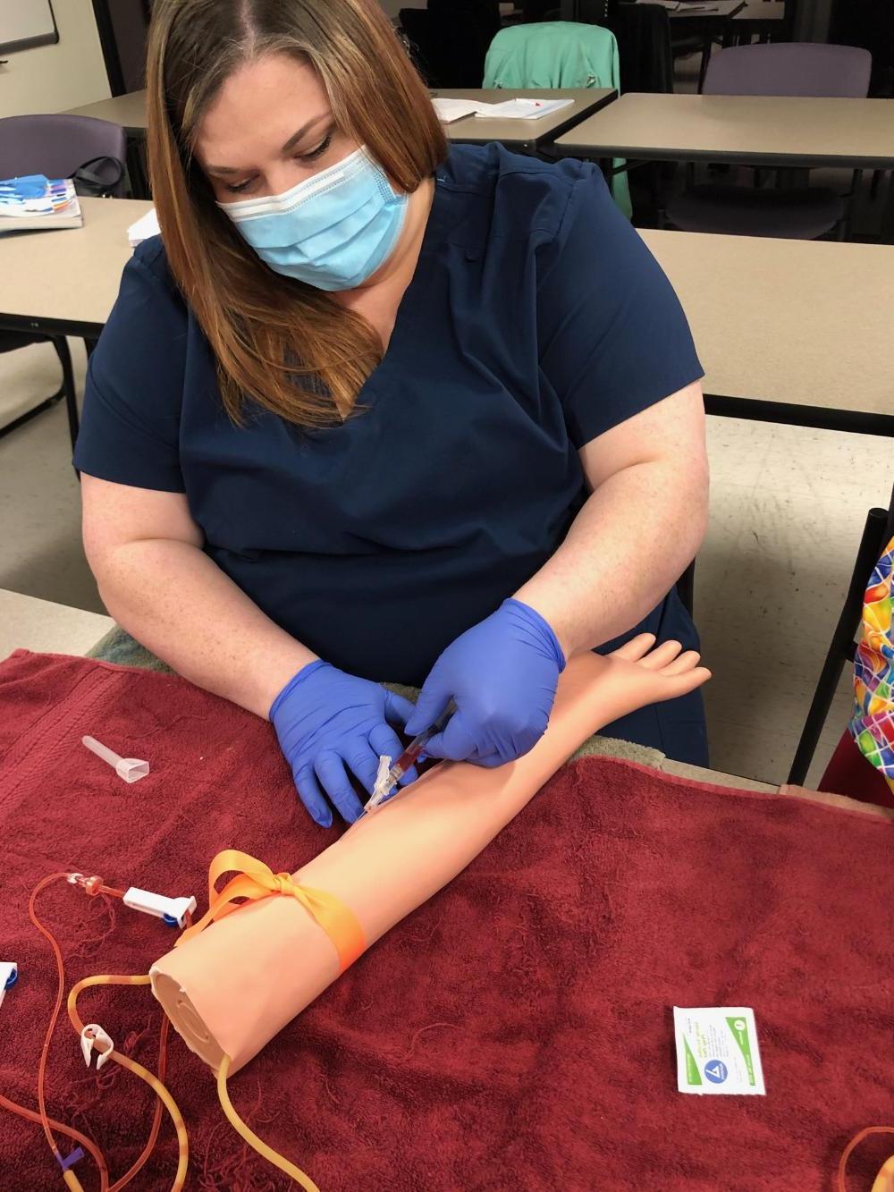 A female student sticking a syringe in a practice arm